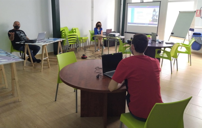 3 personas en un aula con ordenadores y una videollamada proyectada en una pantalla